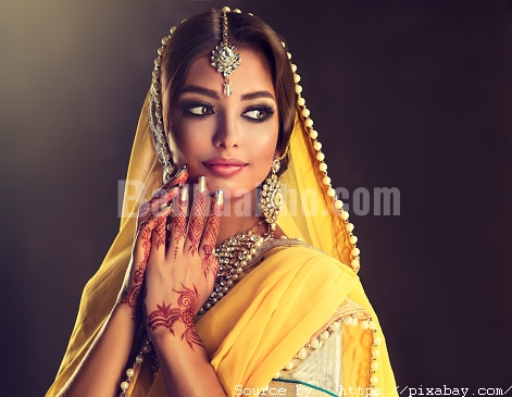 Portrait of beautiful indian girl dressed in a traditional national suit,  mehndi henna tattoo is  painted on her hands and traditional kundan style jewelry set. Black haired indian young woman dressed  in a posh yellow sari costume.